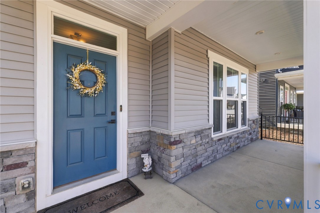 Covered front porch featuring horizontal lap siding, stacked stone veneer wainscoting, a paneled door with a transom window, and integrated recessed lighting Covered front porch featuring horizontal lap siding, stacked stone veneer wainscoting, a paneled door with a transom window, and integrated recessed lighting