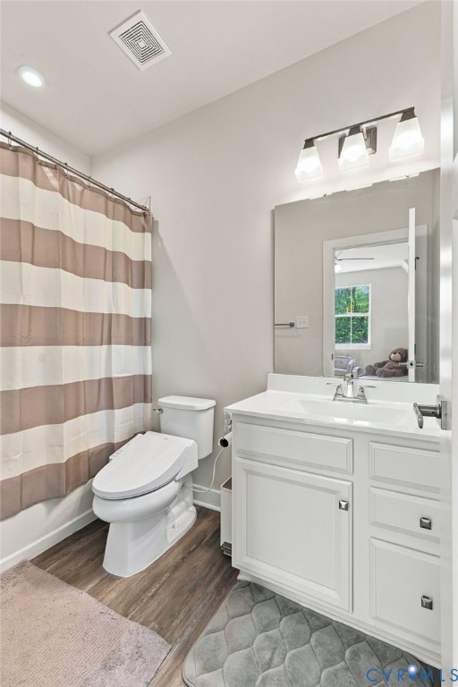 Bathroom featuring a white vanity cabinet with a integrated sink, wood-finish flooring, and a three-light wall-mounted fixture above a rectangular mirror
