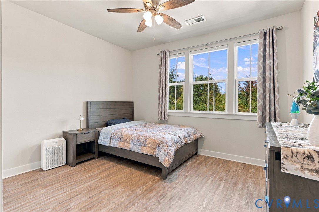Wood-finish flooring, triple-pane window configuration, and a multi-blade ceiling fan with integrated lighting