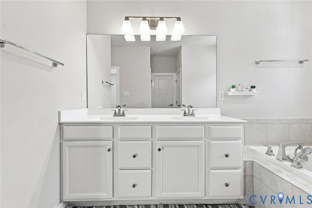 Double vanity with a solid-surface countertop, dual integrated sinks, polished chrome fixtures, and a large wall-mounted vanity mirror featuring four-bulb lighting