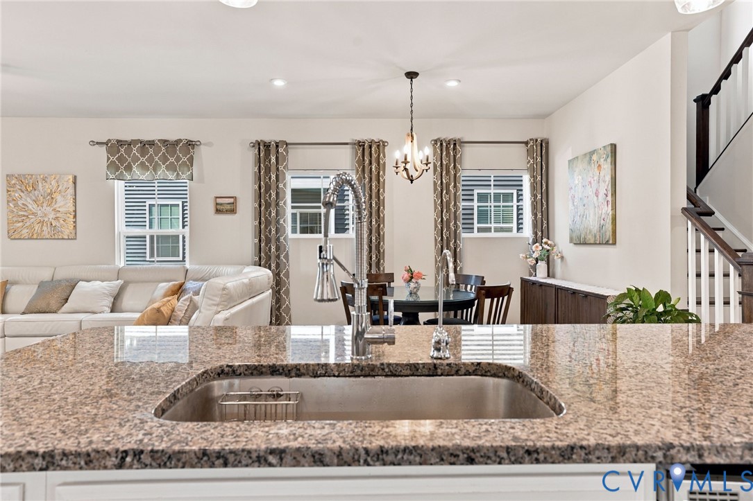 Stone countertop with an undermount sink and high-arc pull-down faucet, featuring a central chandelier, recessed lighting, and a custom built-in cabinetry unit