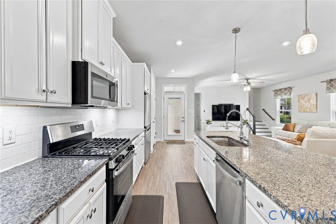 Kitchen featuring white shaker-style cabinetry, stone countertops, a subway tile backsplash, stainless steel appliances, and a central island with an integrated sink Kitchen featuring white shaker-style cabinetry, stone countertops, a subway tile backsplash, stainless steel appliances, and a central island with an integrated sink
