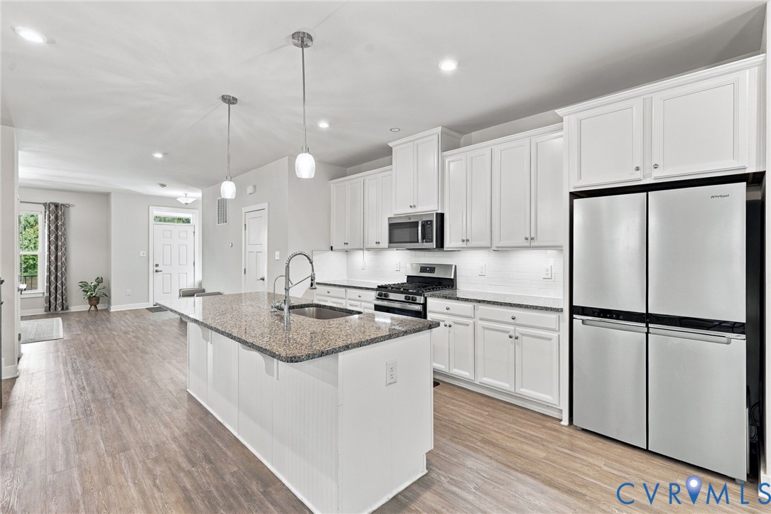 Kitchen featuring white cabinetry, stone-finish countertops, a center island with an integrated sink, stainless steel appliances, and wood-finish flooring