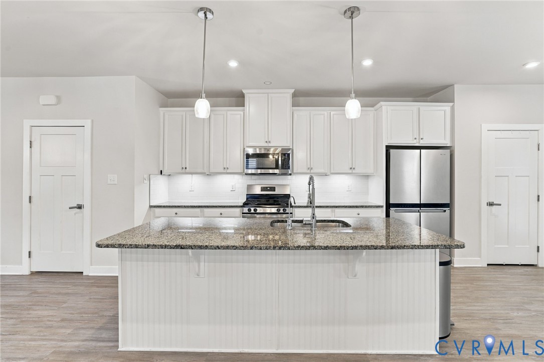 Kitchen featuring white shaker-style cabinetry, stone-finish countertops, a center island with beadboard detailing, stainless steel appliances, and dual pendant lighting