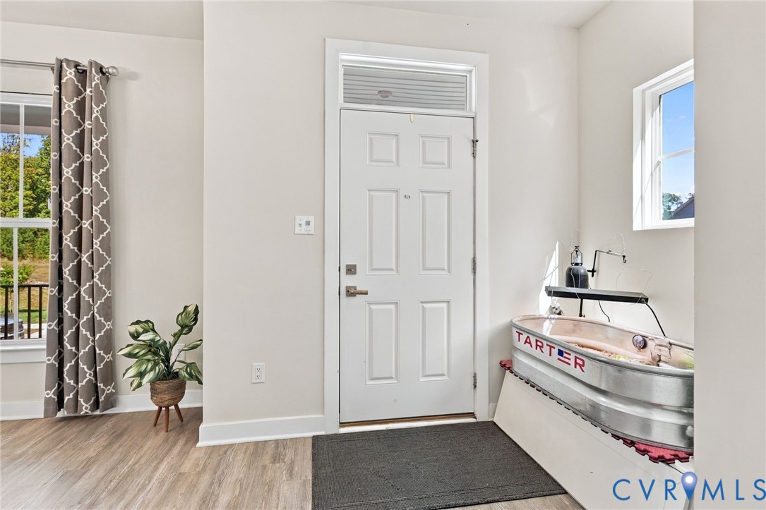 Entryway featuring a white six-panel door with transom window, wood-finish flooring, and multiple windows providing natural light Entryway featuring a white six-panel door with transom window, wood-finish flooring, and multiple windows providing natural light