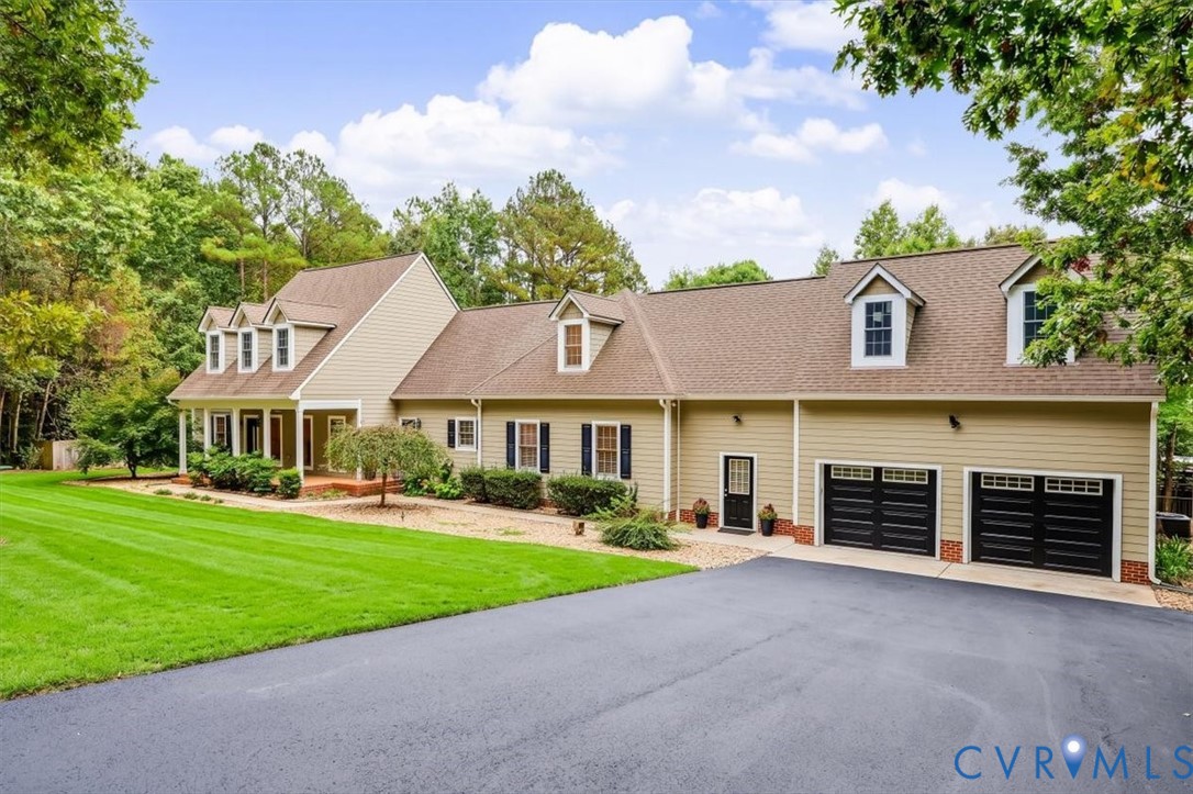 Two-story exterior featuring tan siding, a multi-gabled roofline, dormer windows, an attached two-car garage with black doors, and a paved driveway
