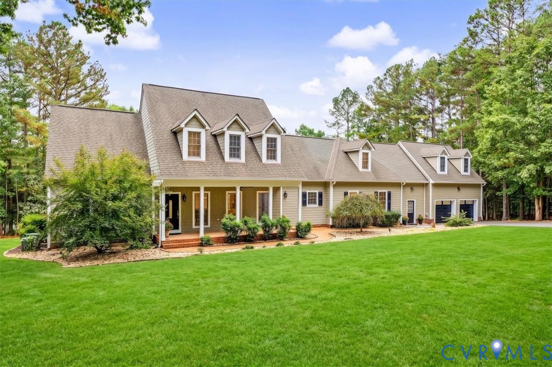 Traditional residence featuring a covered front porch, brick-paver entry, dormer windows, multi-pitched roofline, and an attached two-car garage