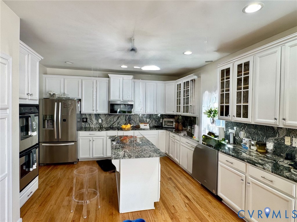 Kitchen featuring white cabinetry, stone countertops, a central island, stainless steel appliances, and wood-finish flooring