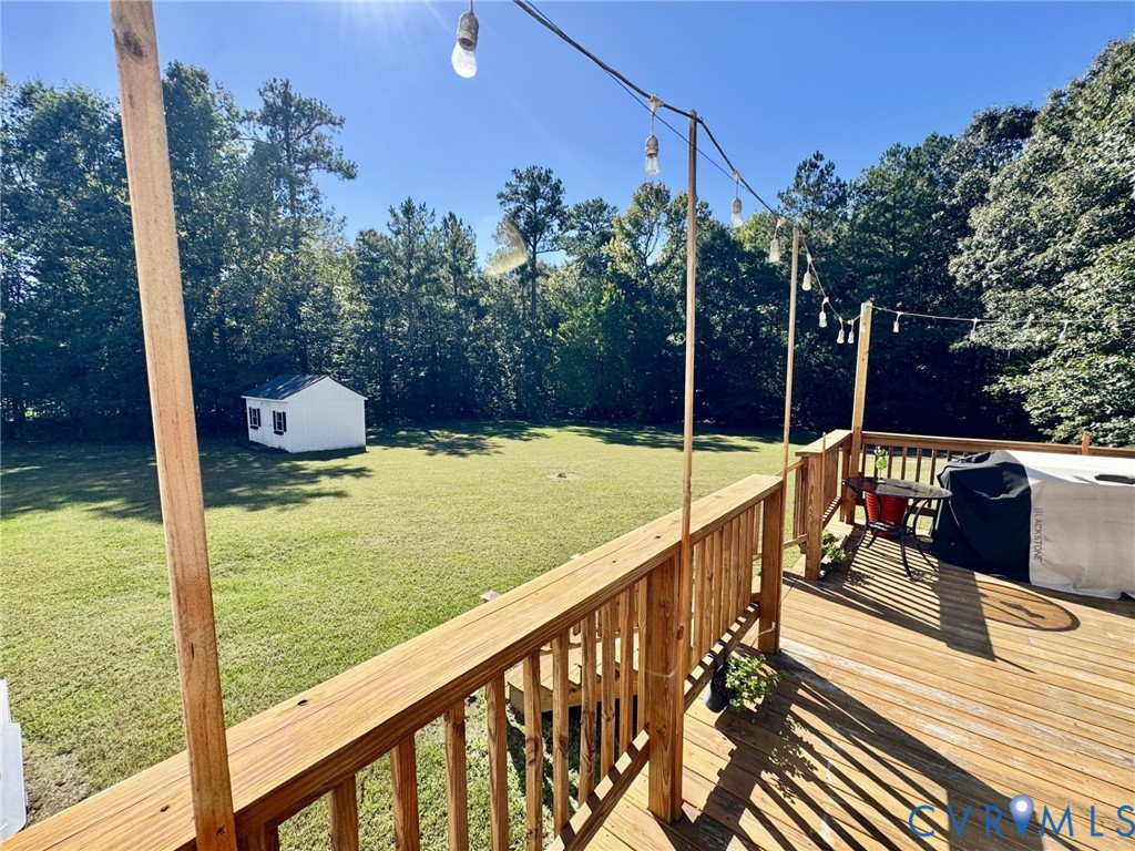 Elevated wood deck featuring a balustrade, integrated string lighting, a spacious backyard, and a detached storage structure