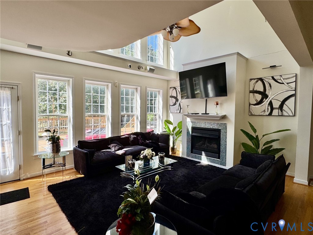 Vaulted ceiling, floor-to-ceiling windows, wood-finish flooring, and a fireplace featuring decorative tile surround