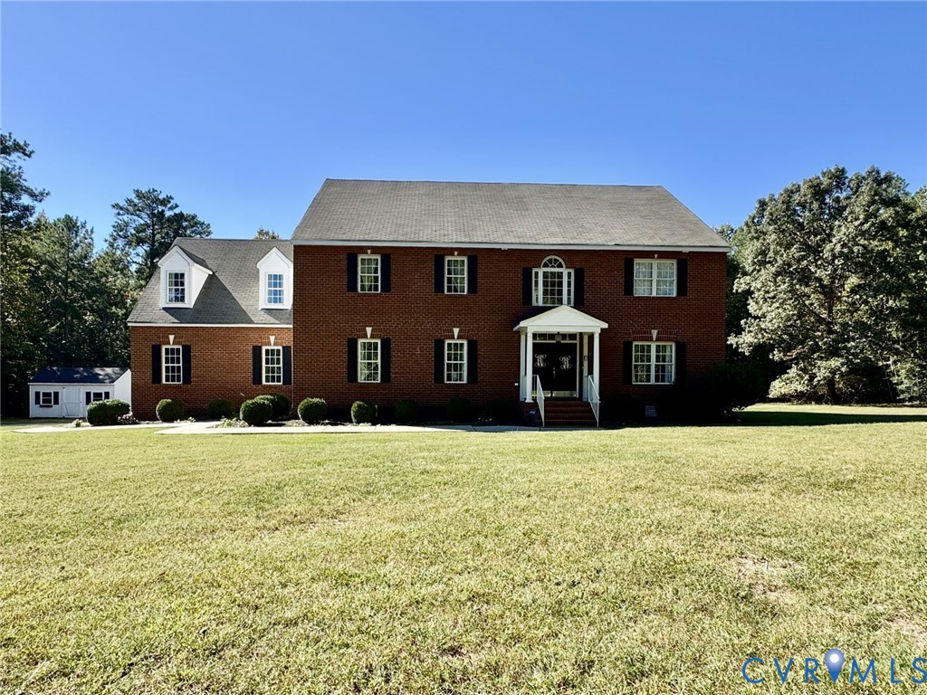 Two-story brick exterior featuring a covered front entryway, symmetrical window placement with shutters, dual dormer windows, and a paved walkway Two-story brick exterior featuring a covered front entryway, symmetrical window placement with shutters, dual dormer windows, and a paved walkway