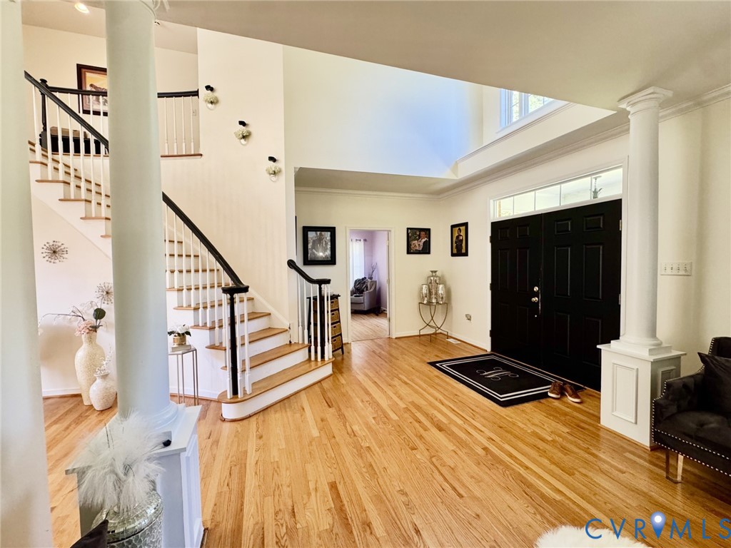 Foyer featuring a two-story ceiling, double front doors with a transom window, wood-finish flooring, and a sweeping staircase with a dark wood handrail