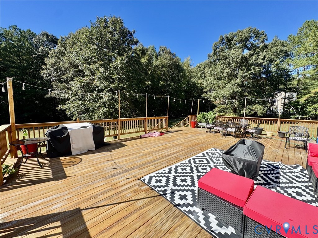 Expansive wood deck featuring a tiered structure, vertical wooden balusters, and a built-in cable lighting system, backed by a perimeter of mature trees
