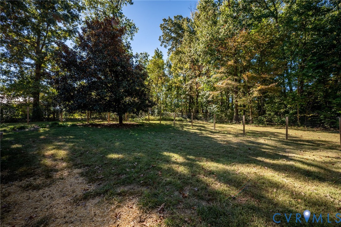 Expansive backyard featuring a level lawn, mature trees, and perimeter post-and-wire fencing