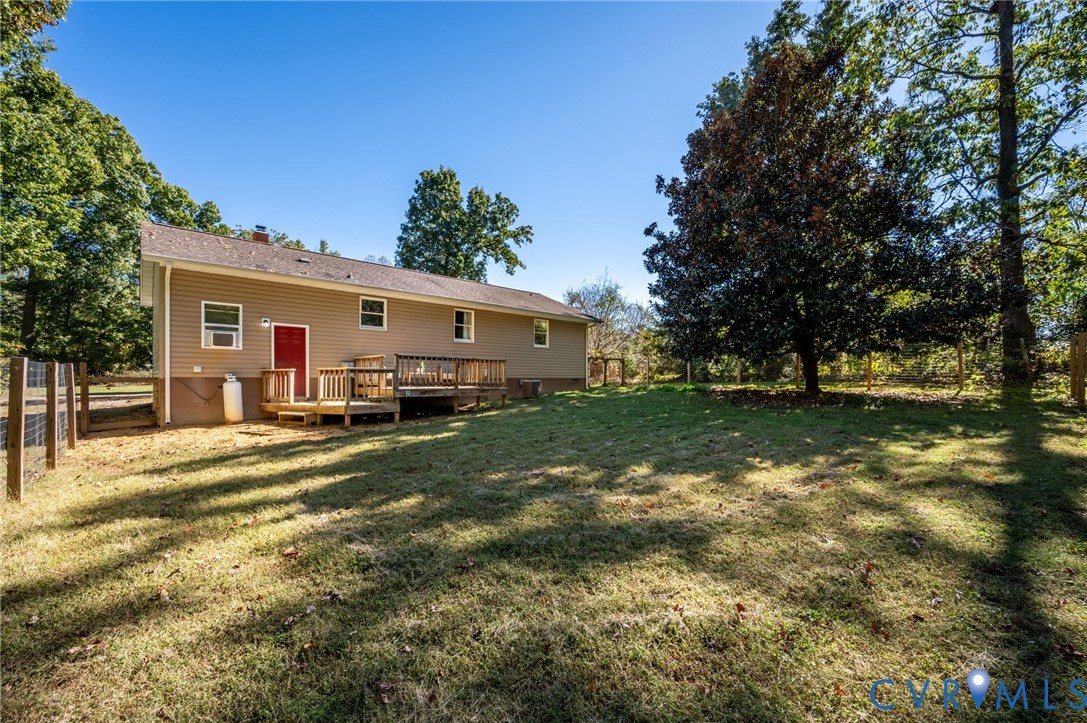 Exterior featuring vinyl siding, a wood deck, and a fenced-in grassy yard with mature trees
