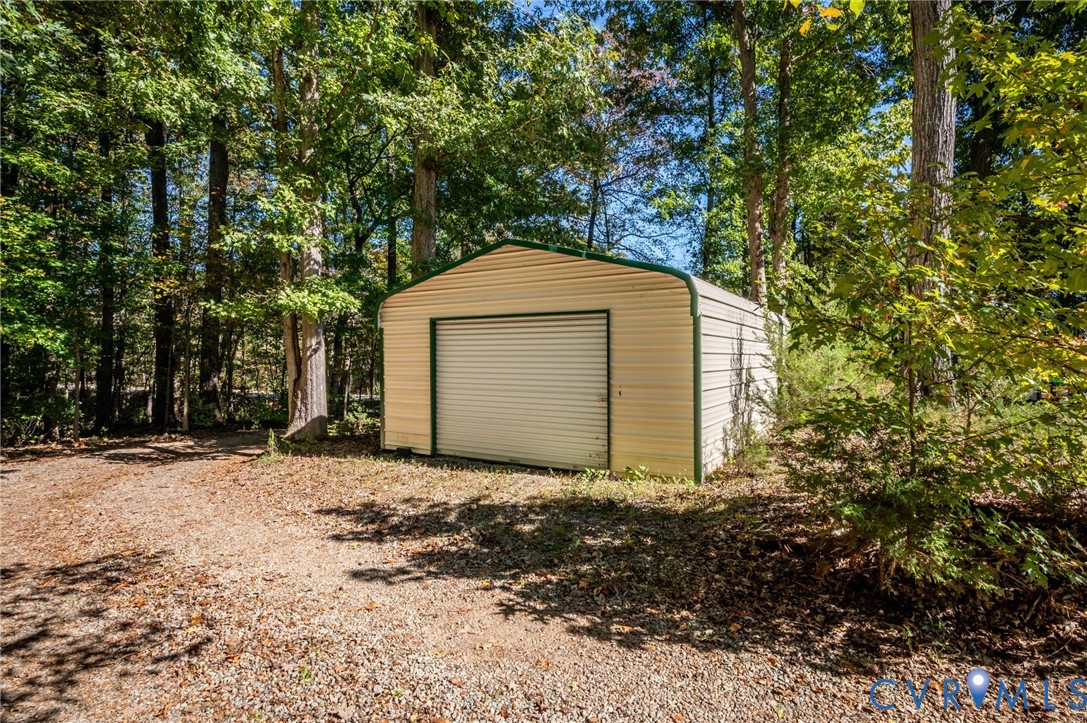 Detached metal storage structure featuring a roll-up door, corrugated siding, and gravel ground surfacing. At front corner of the property and sits away from the house.