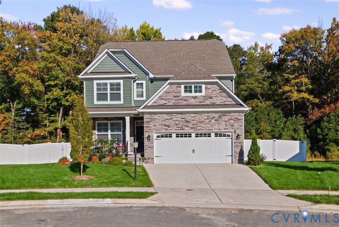 Two-story residence featuring stone veneer siding, horizontal siding, an attached two-car garage, an asphalt shingle roof, and a perimeter vinyl privacy fence Two-story residence featuring stone veneer siding, horizontal siding, an attached two-car garage, an asphalt shingle roof, and a perimeter vinyl privacy fence