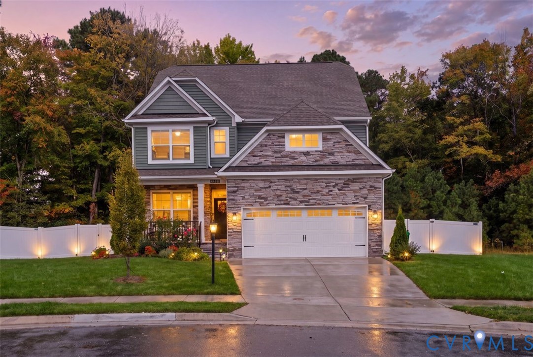 Two-story residence featuring a stone veneer facade, horizontal lap siding, attached two-car garage, concrete driveway, and a perimeter vinyl privacy fence