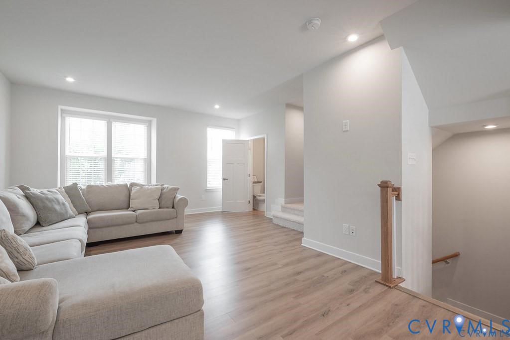 Open-concept area featuring wood-finish flooring, recessed lighting, double-hung windows, and a wood-capped staircase railing