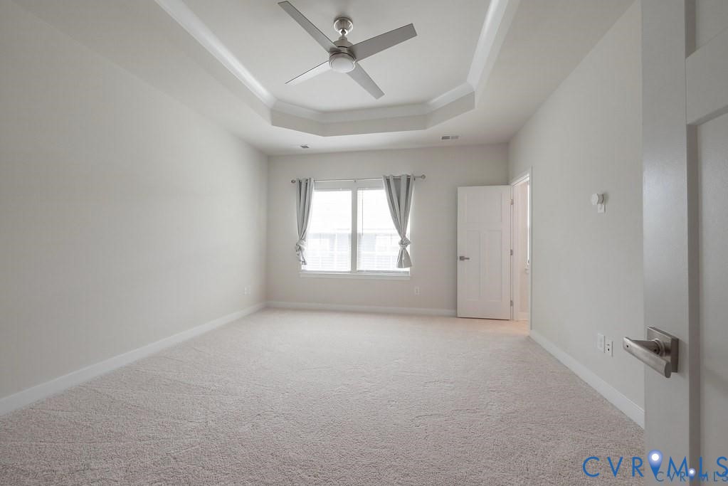 Tray ceiling featuring a central brushed-metal ceiling fan, wall-to-wall carpeting, and a multi-panel door