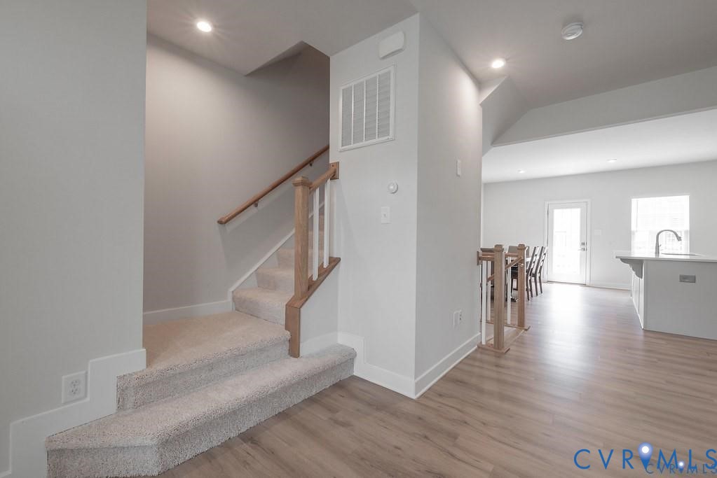 Staircase featuring carpeted steps, a wooden handrail, and white balusters, finished with wood-finish flooring and recessed lighting