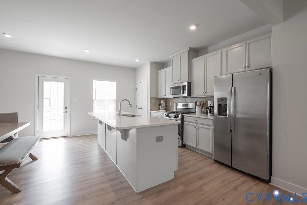 Kitchen featuring wood-finish flooring, white cabinetry, a center island with a stone-surface countertop, and stainless steel appliances