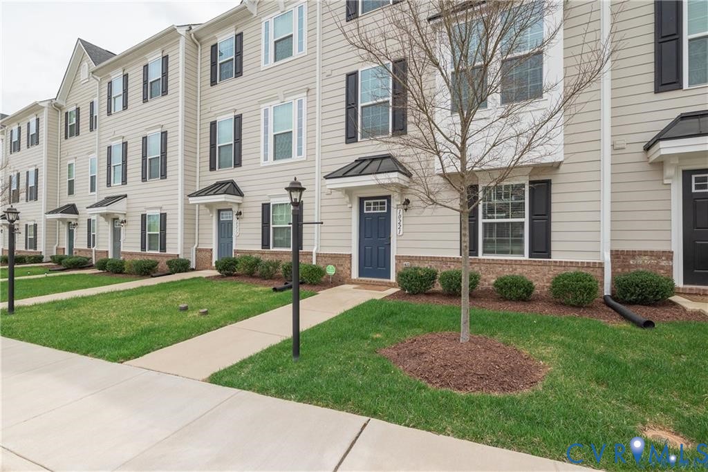 Multi-story exterior featuring horizontal siding, brick veneer foundation, metal-accented door awnings, and black decorative shutters