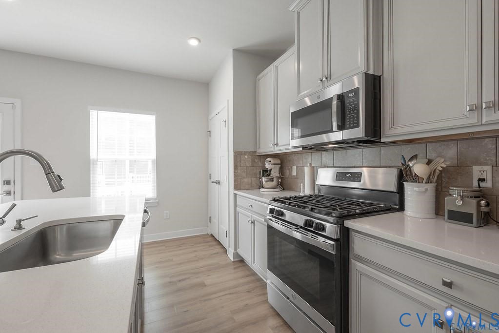 Kitchen featuring shaker-style cabinetry, quartz countertops, tile backsplash, stainless steel appliances, and wood-finish flooring