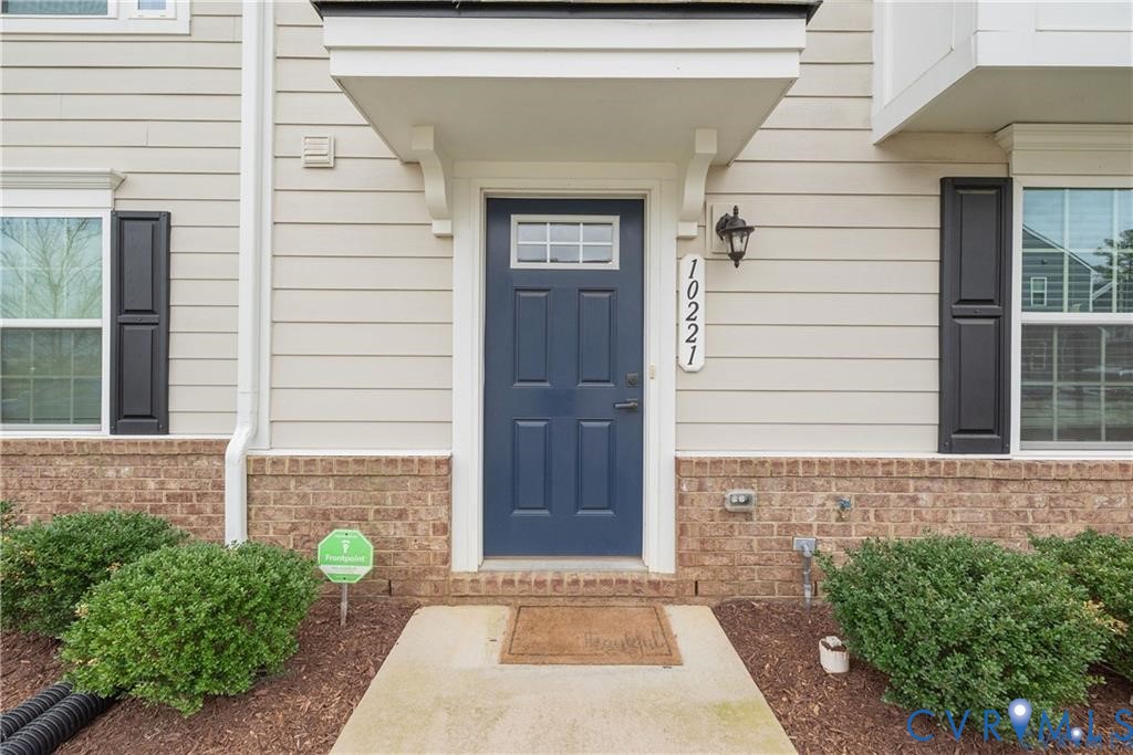 Entrance featuring a navy-painted door with transom window, lap siding, brick facade accents, and decorative window shutters