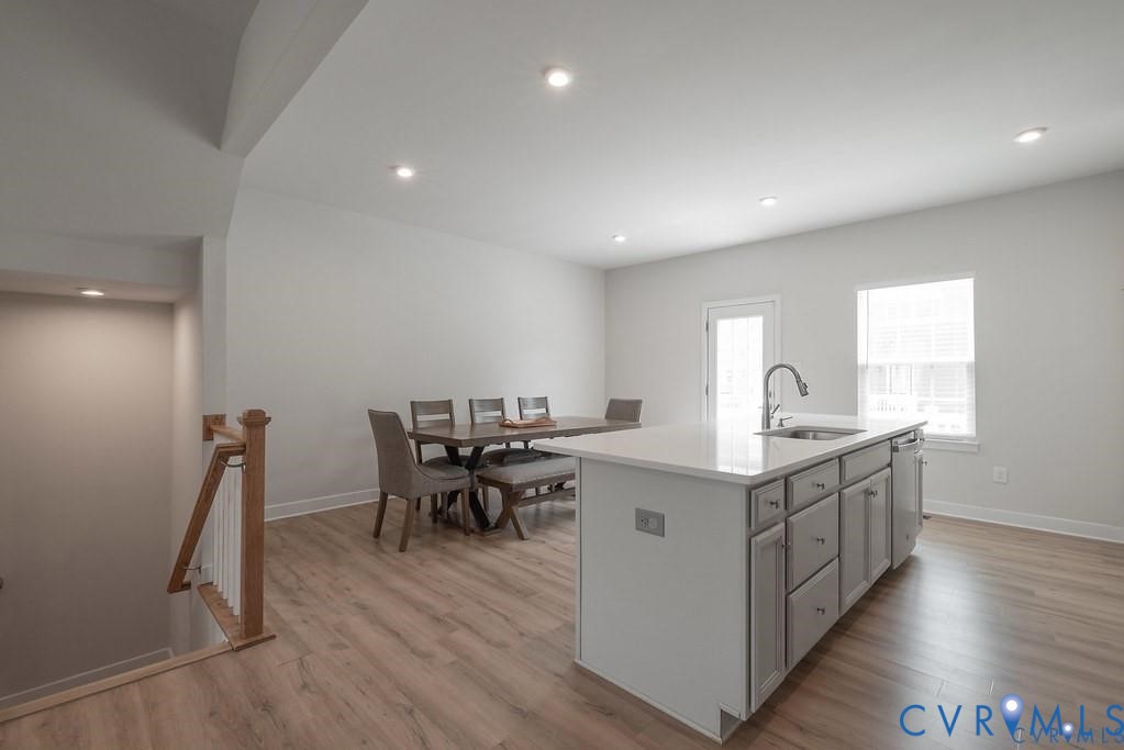 Kitchen featuring a central island with a solid surface countertop, stainless steel undermount sink, recessed lighting, and wood-finish flooring