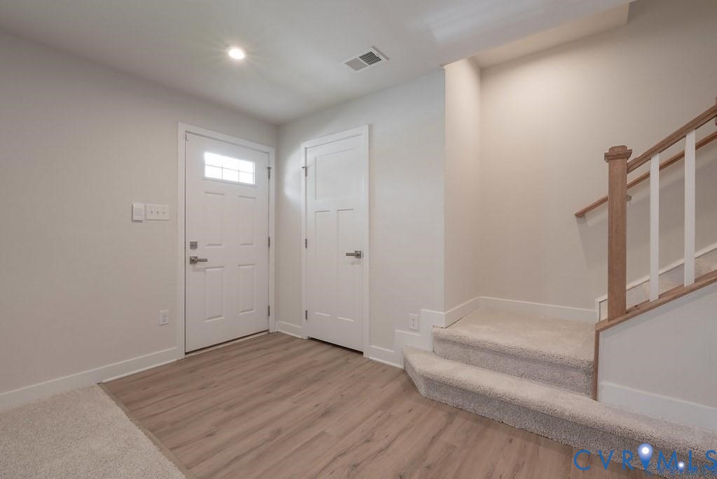 Entryway featuring a white paneled exterior door with a glass inlay, wood-finish flooring, and a staircase with a stained wood handrail and white balusters
