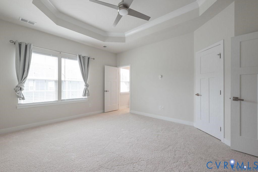 Tray ceiling with a centered ceiling fan, neutral wall paint, carpeting, and multi-panel interior doors