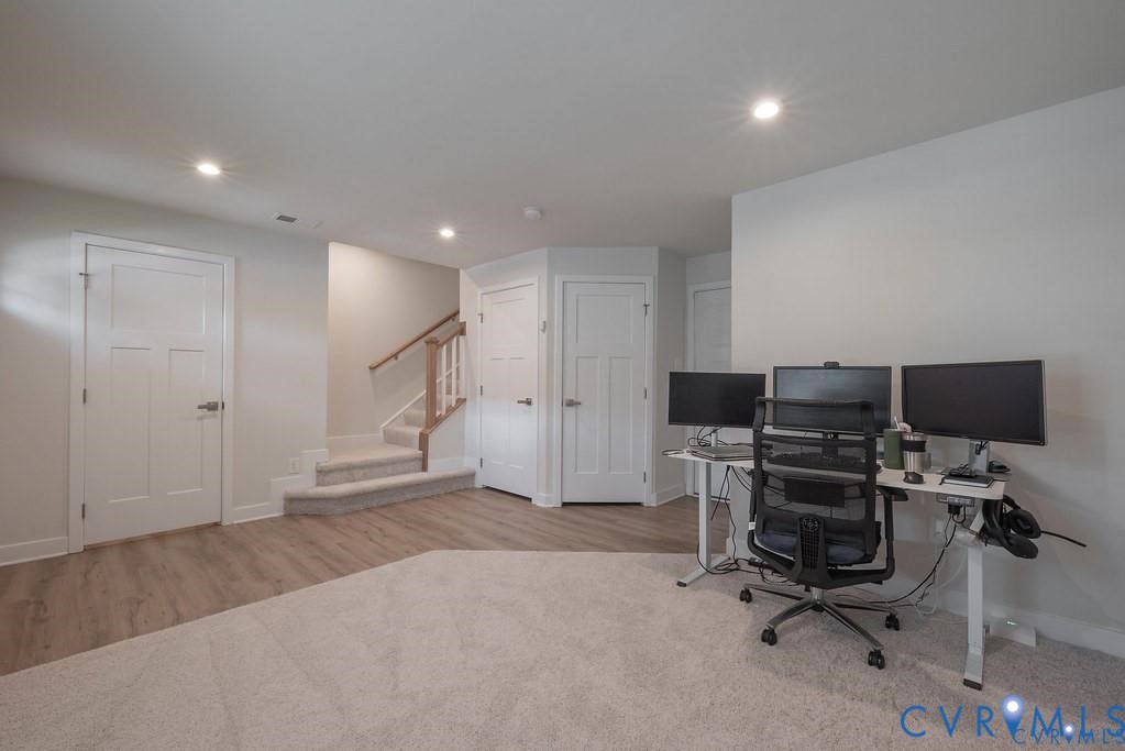 Neutral-toned interior featuring wood-finish flooring, wall-to-wall carpeting, three-panel interior doors, recessed lighting, and a staircase with a wooden handrail