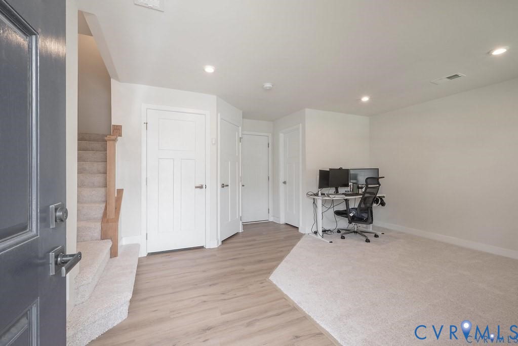 Interior space featuring wood-finish flooring, recessed lighting, carpeted staircase with wood-capped railing, and multiple panel doors