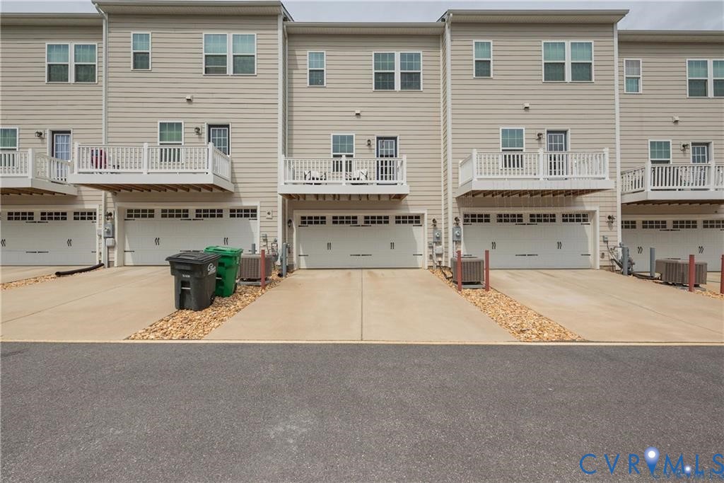 Multi-level townhome exterior featuring light-toned horizontal siding, private raised decks with white railings, concrete driveways, and two-car attached garages