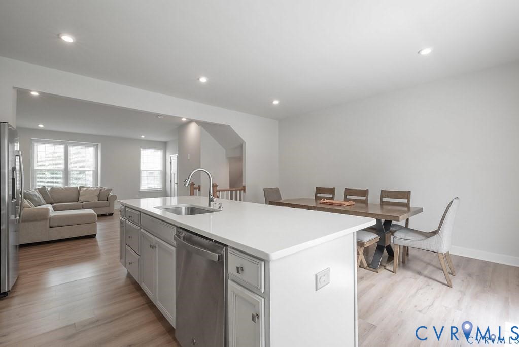 Kitchen featuring a central island with white cabinetry, light-toned stone-finish countertop, stainless steel dishwasher, and a gooseneck faucet, set against wood-finish flooring and recessed lighting