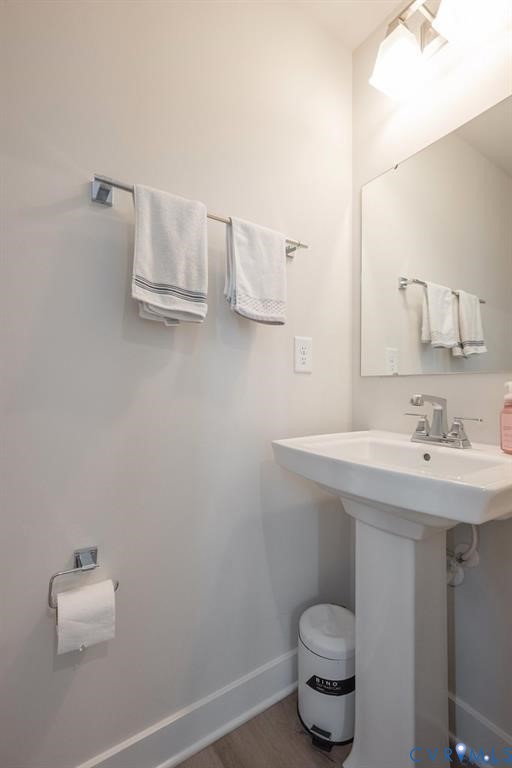 Pedestal sink with a polished chrome faucet, rectangular wall-mounted mirror, brushed nickel towel bar, and wood-finish flooring