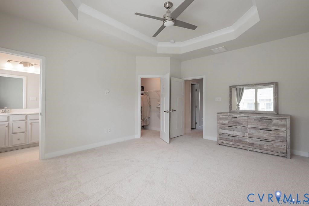 Tray ceiling with recessed lighting and neutral wall-to-wall carpeting, featuring a mounted ceiling fan and interior doors with panel detailing