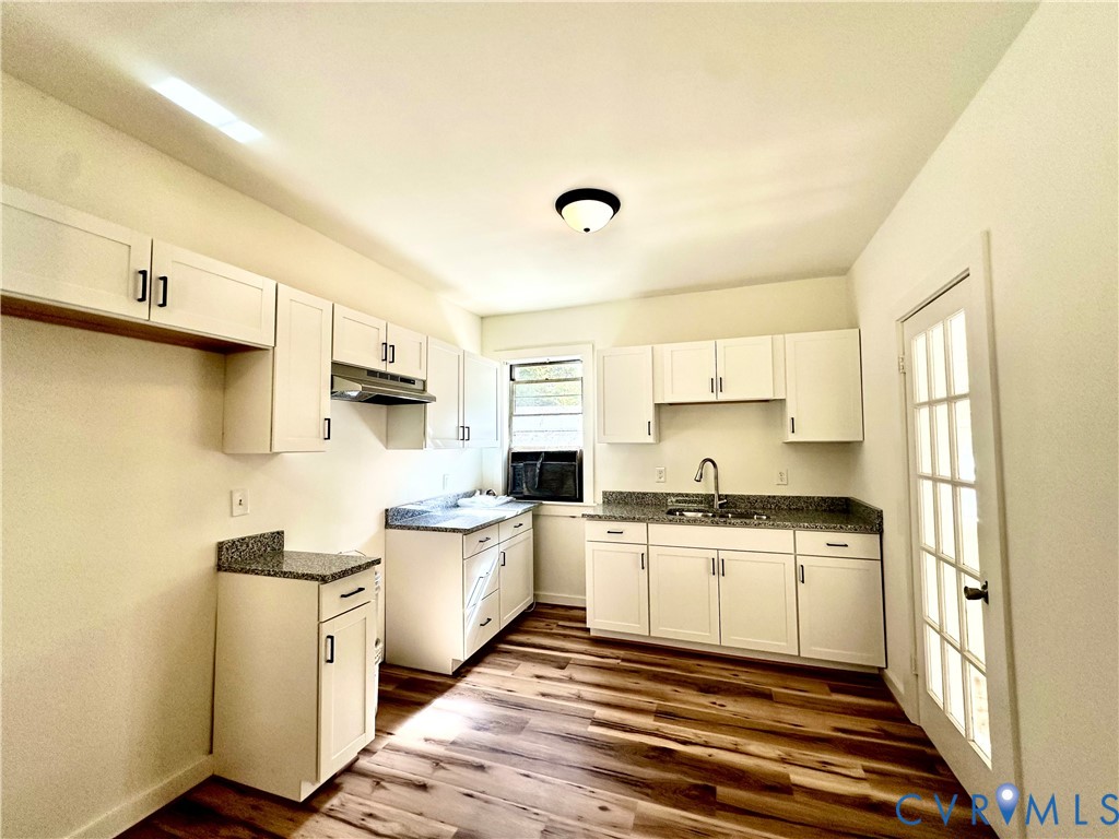 Kitchen featuring white shaker-style cabinetry, stone-finish countertops, wood-finish flooring, a stainless steel sink with a gooseneck faucet, and a multi-pane glass door