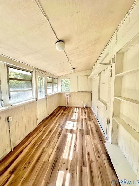 Enclosed porch featuring wood-finish flooring, painted vertical wood wall paneling, built-in shelving, and multiple windows