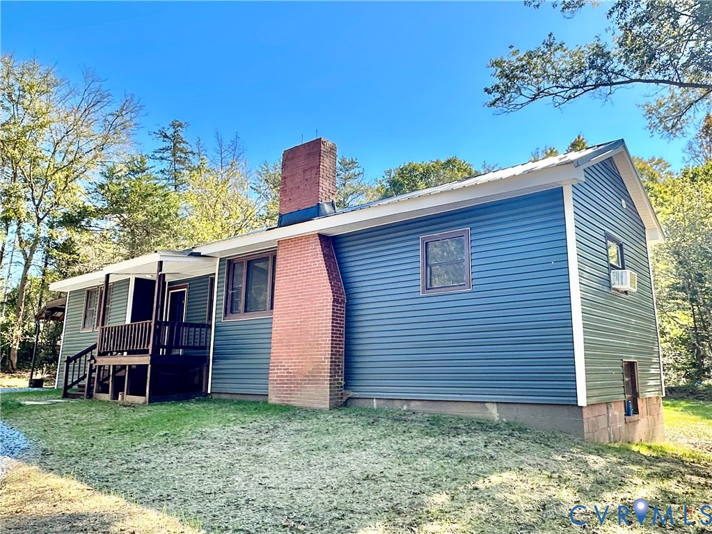 Blue vinyl siding exterior featuring an exposed brick chimney, metal roof, and an attached elevated wooden porch