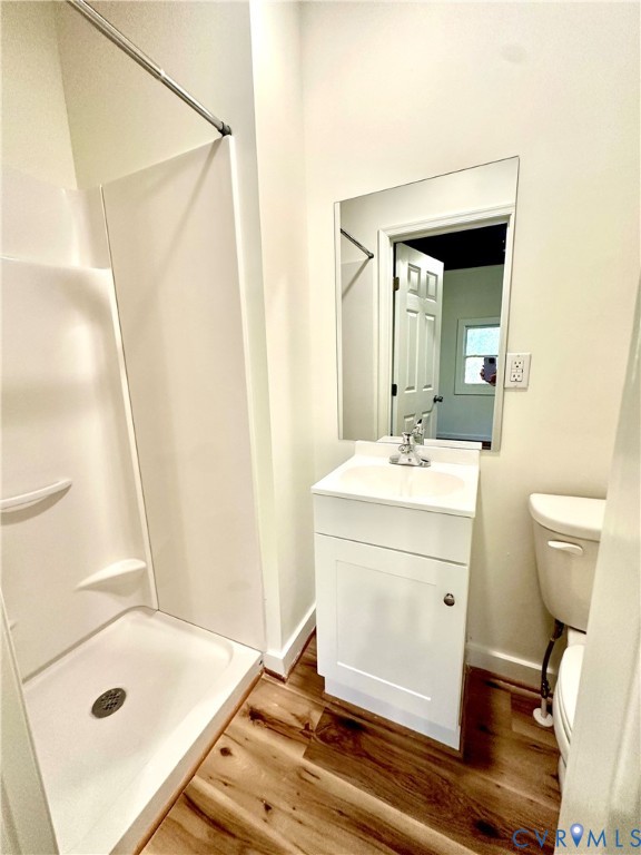 Bathroom featuring a shower stall with a molded surround, white vanity cabinet with an integrated sink, rectangular frameless mirror, and wood-finish flooring