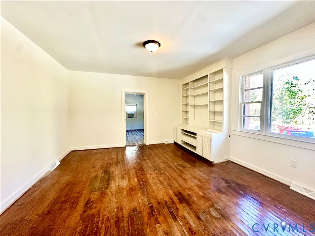 Room featuring wood-finish flooring, built-in floor-to-ceiling shelving, and large window