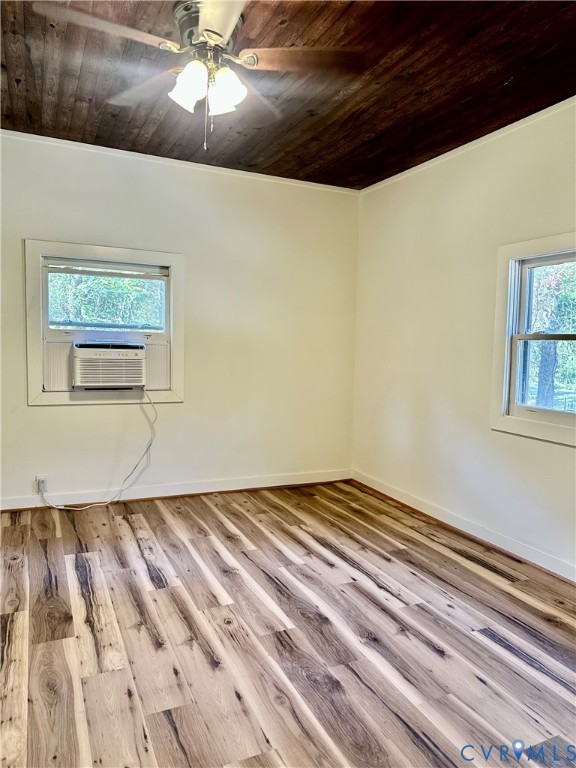 Room interior featuring wood-finish flooring, a dark-stained wood-paneled ceiling, and a ceiling-mounted light fixture with a central fan