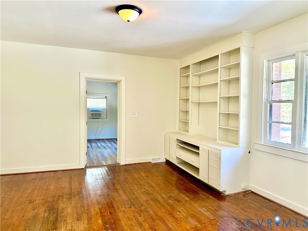 Room interior featuring hardwood flooring, built-in floor-to-ceiling shelving with cabinetry, and a flush-mount ceiling light fixture