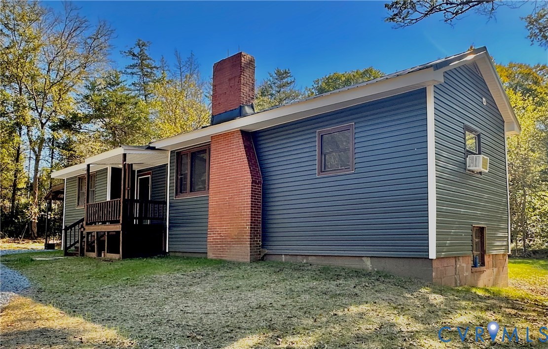 Exterior featuring dark horizontal siding, a prominent exposed red brick chimney, and a raised wooden porch with railings