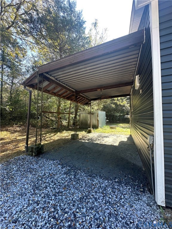 Attached carport featuring a metal roof, dark horizontal siding, and gravel ground surfacing