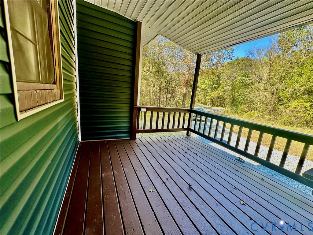Covered porch featuring dark wood-finish decking, horizontal vinyl siding, and wooden railings