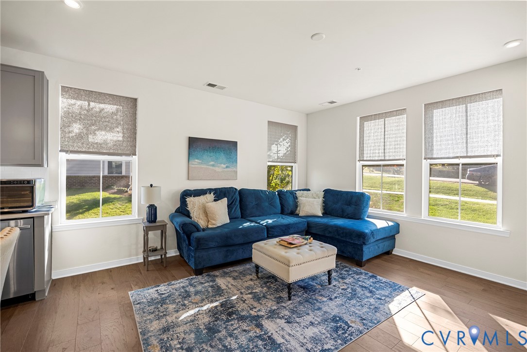 Open-concept living space featuring wood-finish flooring, recessed lighting, and multiple windows with integrated shades