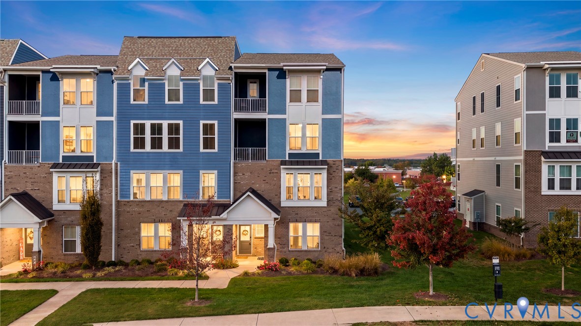 Multi-story exterior featuring blue siding, brick masonry, gabled rooflines, recessed balconies, and manicured landscaping